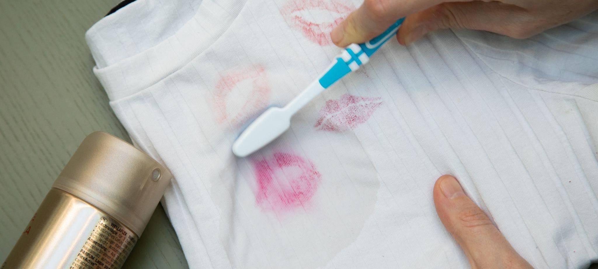 Mit einer Zahnbürste wird ein Lippenstiftfleck vom Shirt entfernt