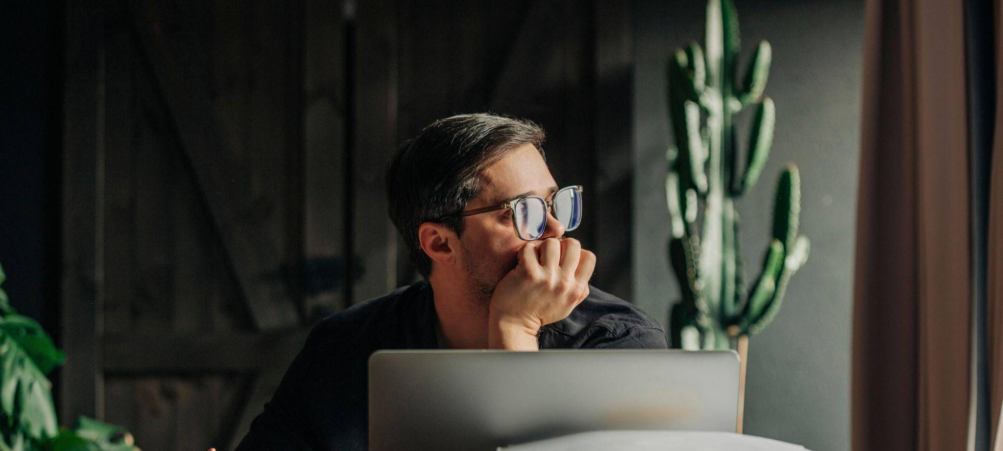 Ein Mann arbeitet am Laptop und sieht aus dem Fenster